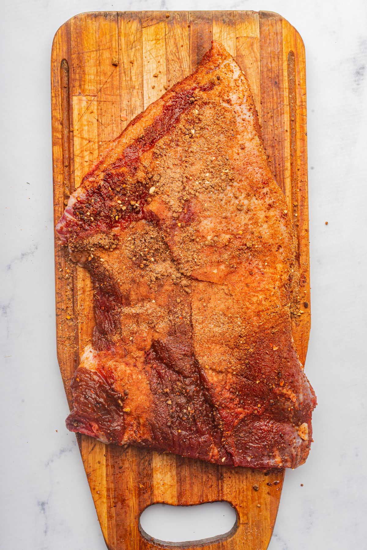 Brisket seasoned with BBQ dry rub on a cutting board.