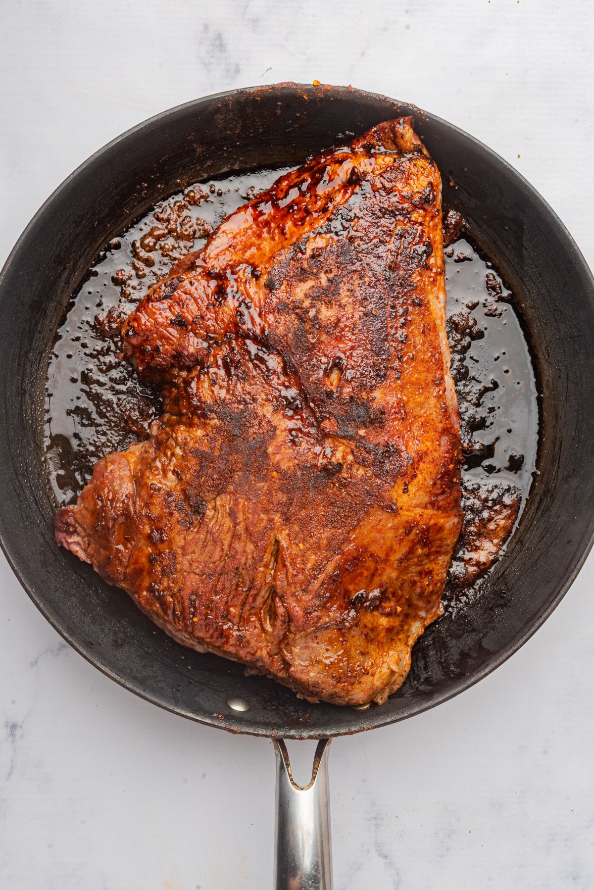 Beef brisket seared in a large skillet.