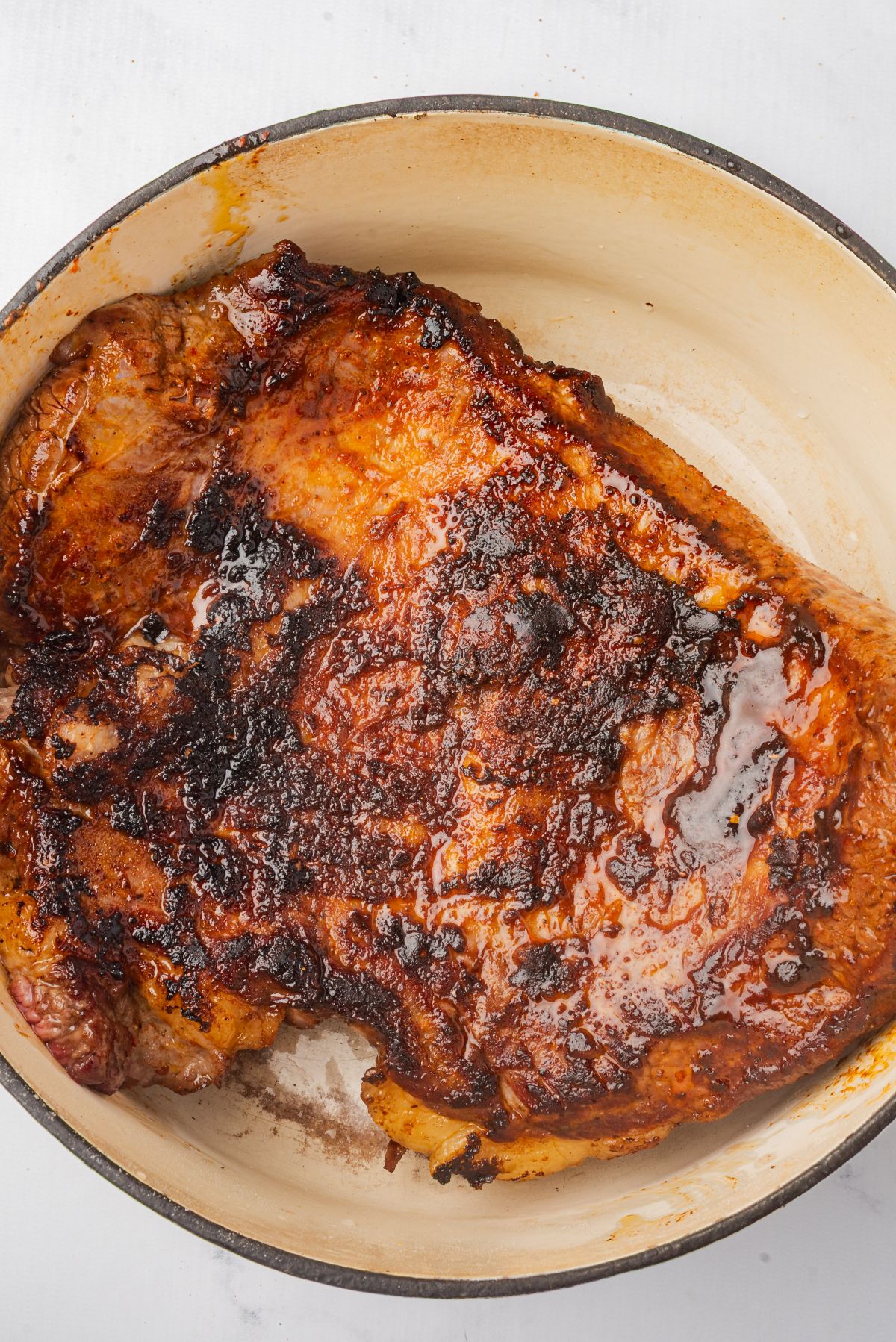 A large Dutch oven pot with a seared brisket placed inside.