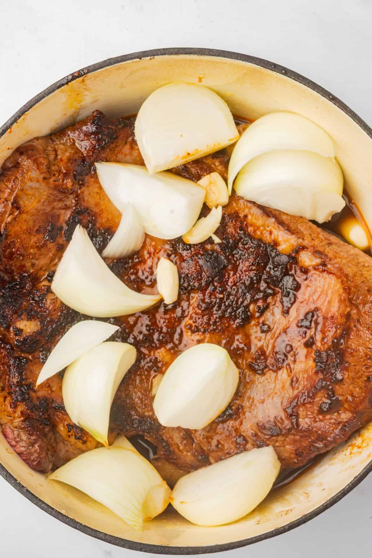 Beef brisket in a Dutch oven with braising liquid, garlic, and onions.