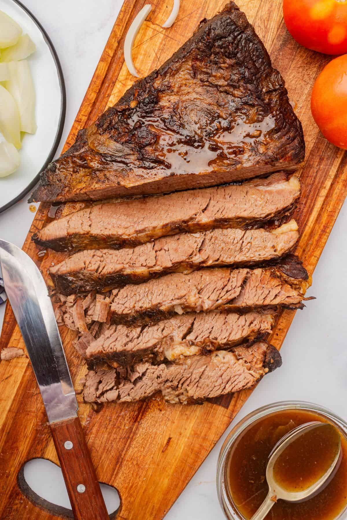 Braised beef brisket sliced on a cutting board with a knife.