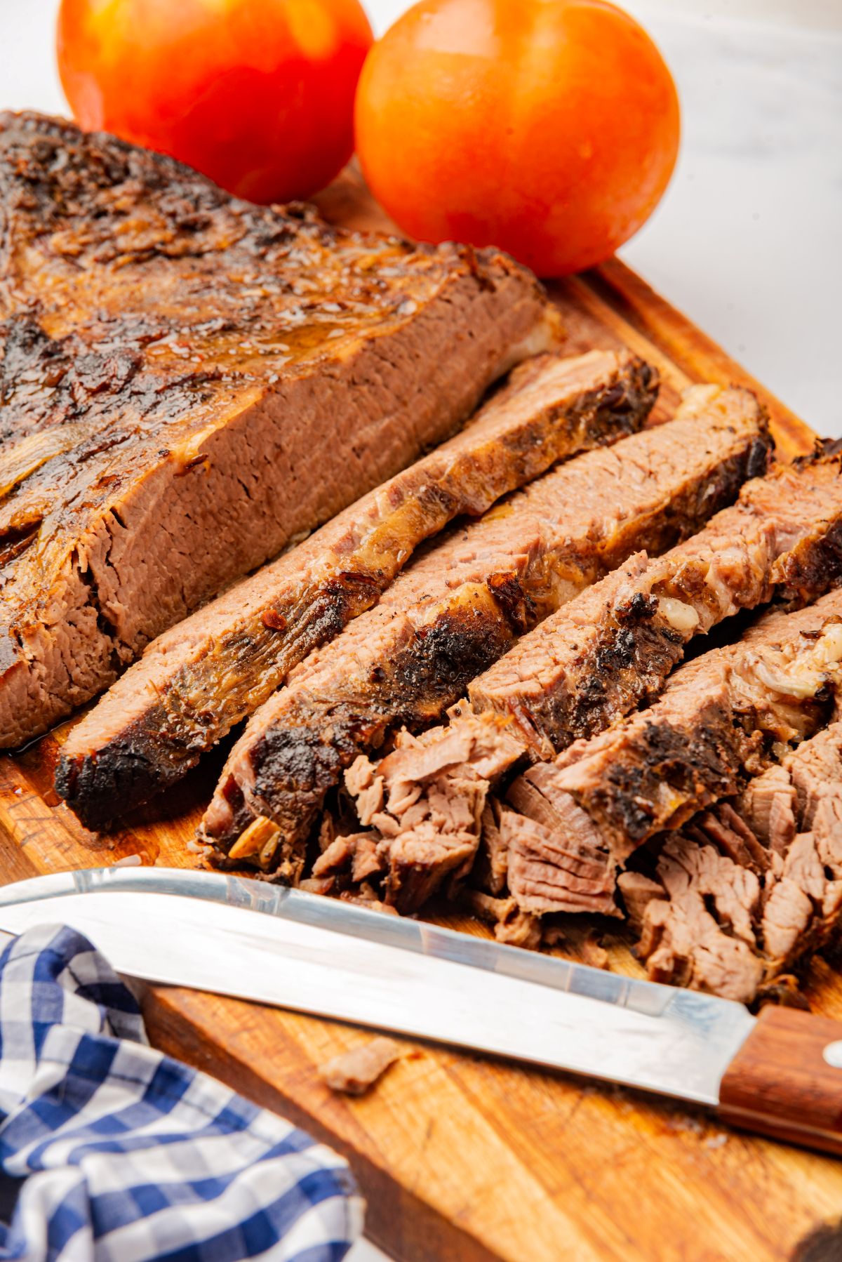 Dutch oven cooked brisket sliced on a cutting board with a knife.