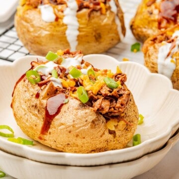 A loaded baked potato with brisket, BBQ sauce, cheese, and sour cream on a plate.