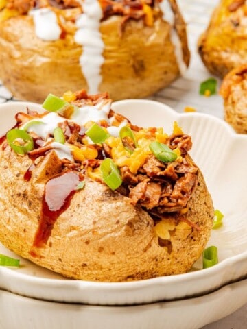 A loaded baked potato with brisket, BBQ sauce, cheese, and sour cream on a plate.