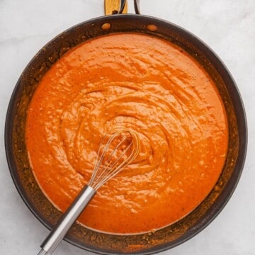 Red enchilada sauce recipe in a saucepan with a whisk.