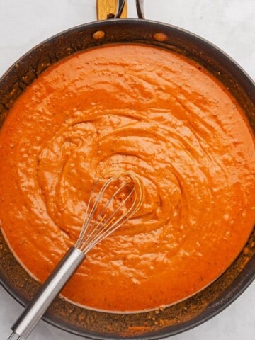 Red enchilada sauce recipe in a saucepan with a whisk.