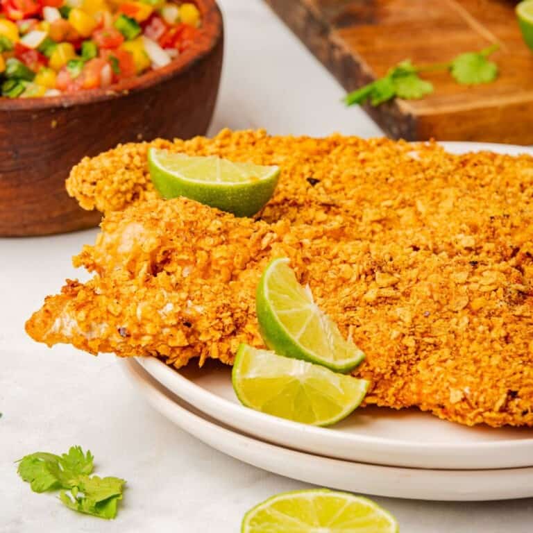 Tortilla crusted tilapia on a plate with lime wedges.