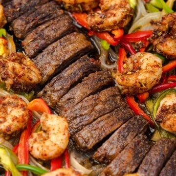Sliced steak and shrimp fajitas with peppers on a sheet pan.