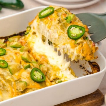 Chicken enchiladas with green sauce in a casserole dish topped with melted cheese and peppers.