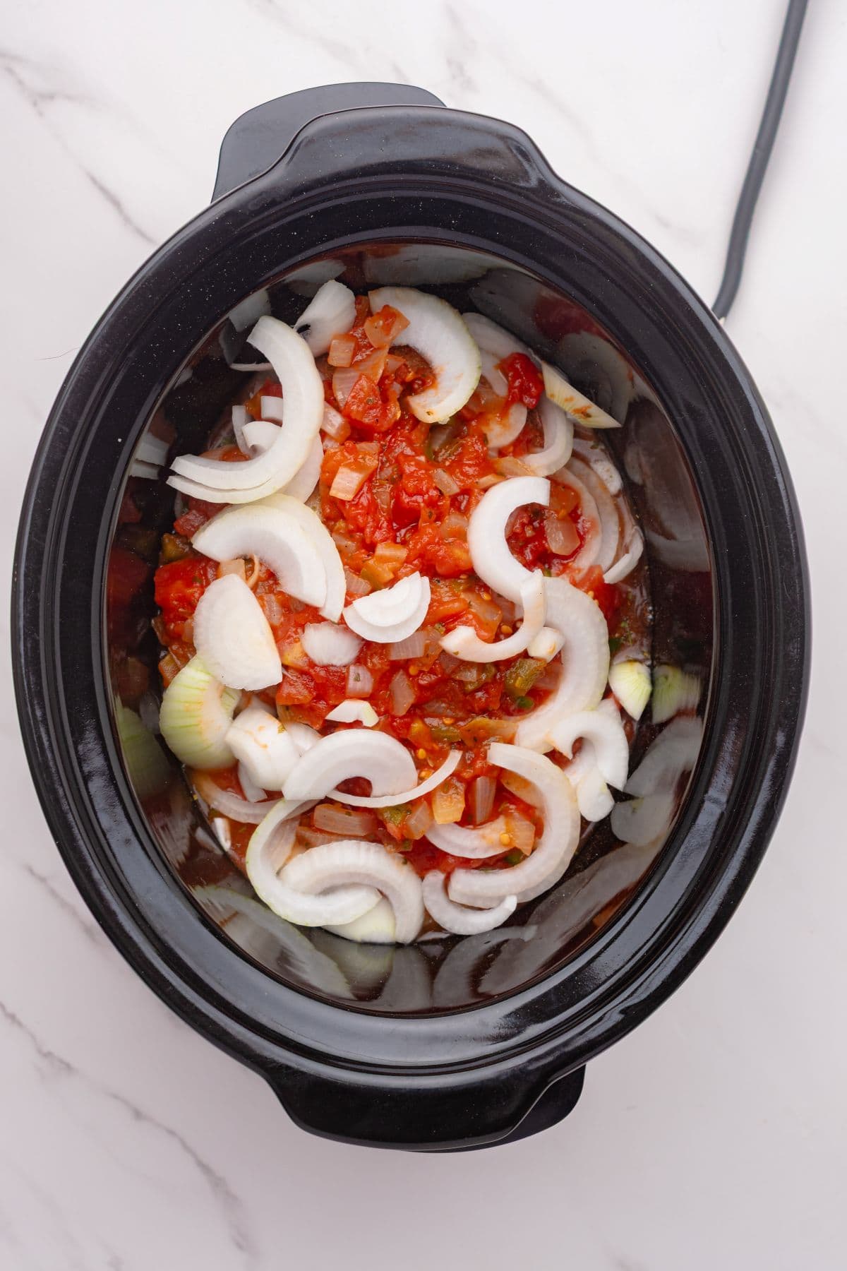 Chicken with salsa and onions are in a slow cooker.