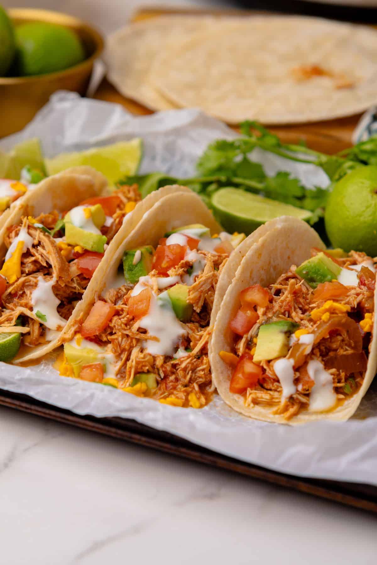 Three shredded chicken tacos wrapped in flour tortillas with salsa and taco toppings.