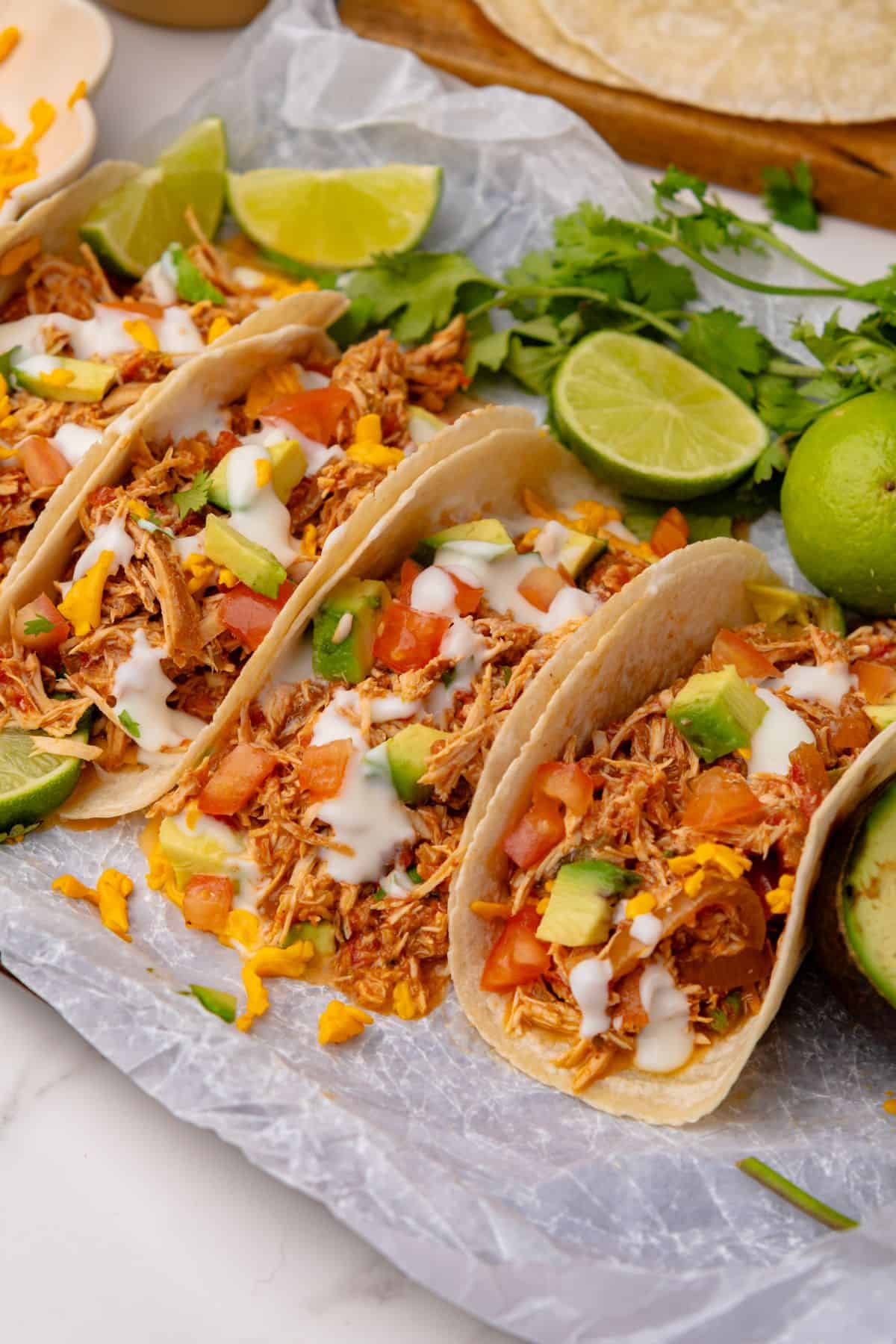 Slow cooker chicken tacos with salsa, diced tomatoes, avocado, shredded cheese, and sour cream.