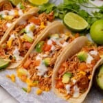Slow cooker chicken tacos with salsa, diced tomatoes, avocado, shredded cheese, and sour cream.