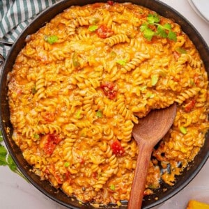 Cheesy taco pasta cooked in one pot being stirred with a wooden spoon.