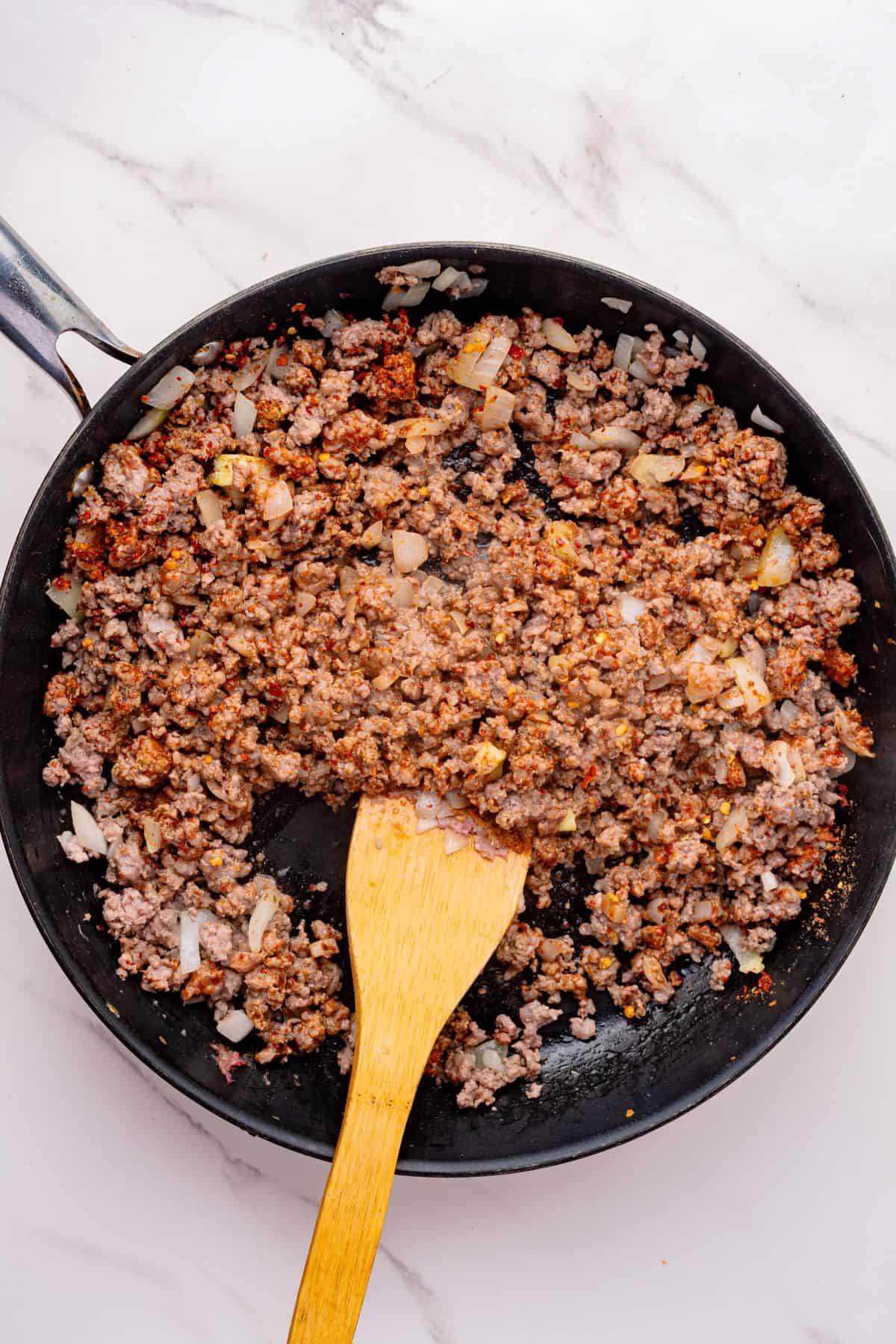 Ground beef with taco seasoning cooking in a skillet with a wooden spoon.
