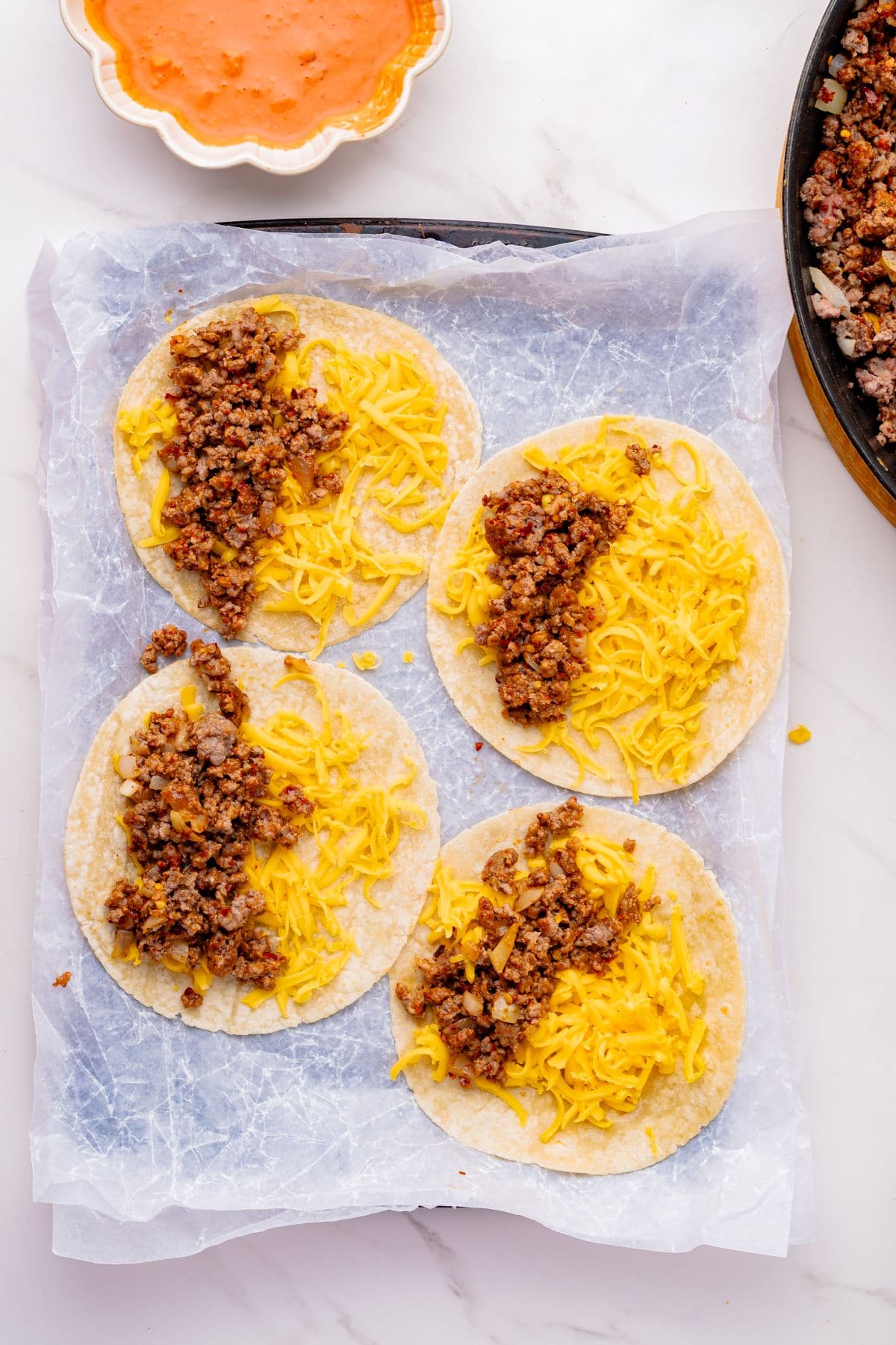 Open faced corn tortillas with ground beef and cheese on a sheet pan.