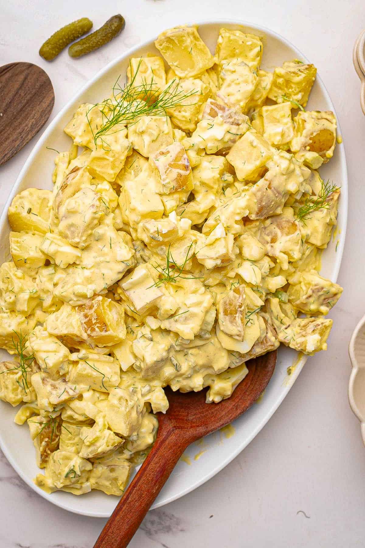 Mustard potato salad on a platter with a wooden spoon.