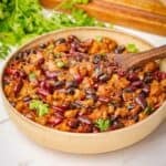 Cowboy baked beans in a bowl with a wooden spoon.