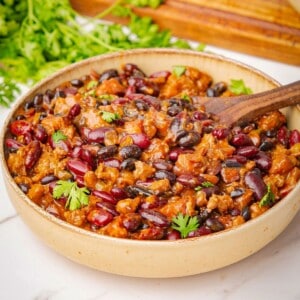 Cowboy baked beans in a bowl with a wooden spoon.