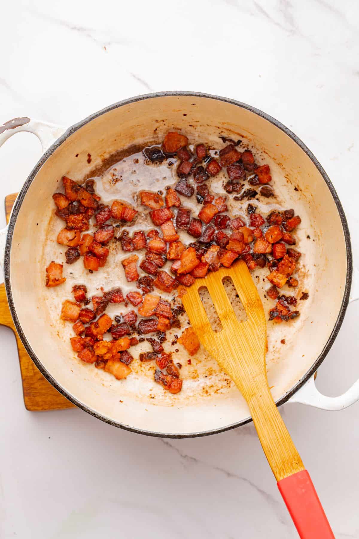 Bacon pieces cooking in a Dutch oven.