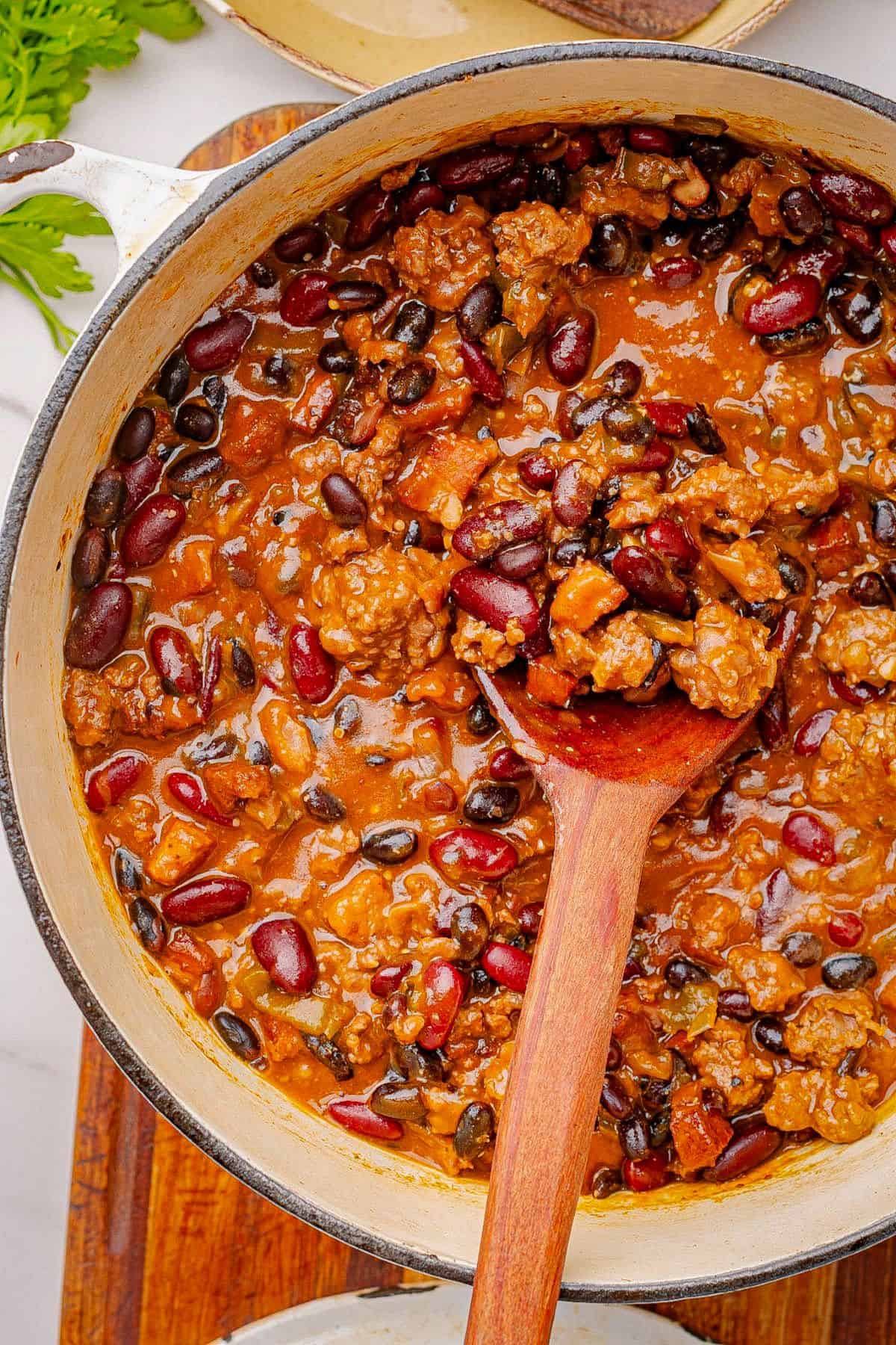 Baked beans with ground beef and bacon in a Dutch oven with a wooden spoon.