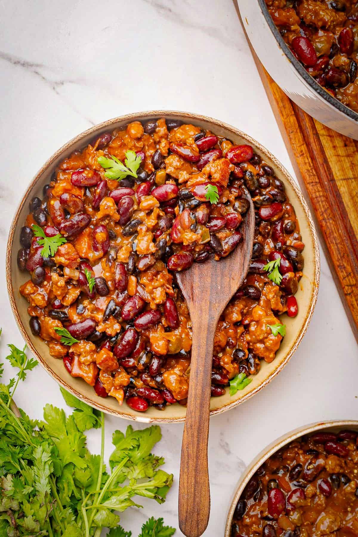 Cowboy baked beans with beef and bacon in a bowl with a wooden spoon.