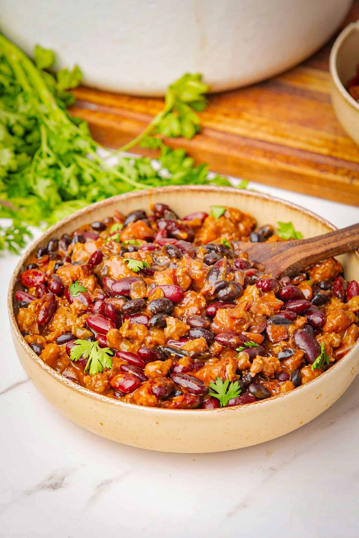 Cowboy baked beans in a bowl with a wooden spoon.