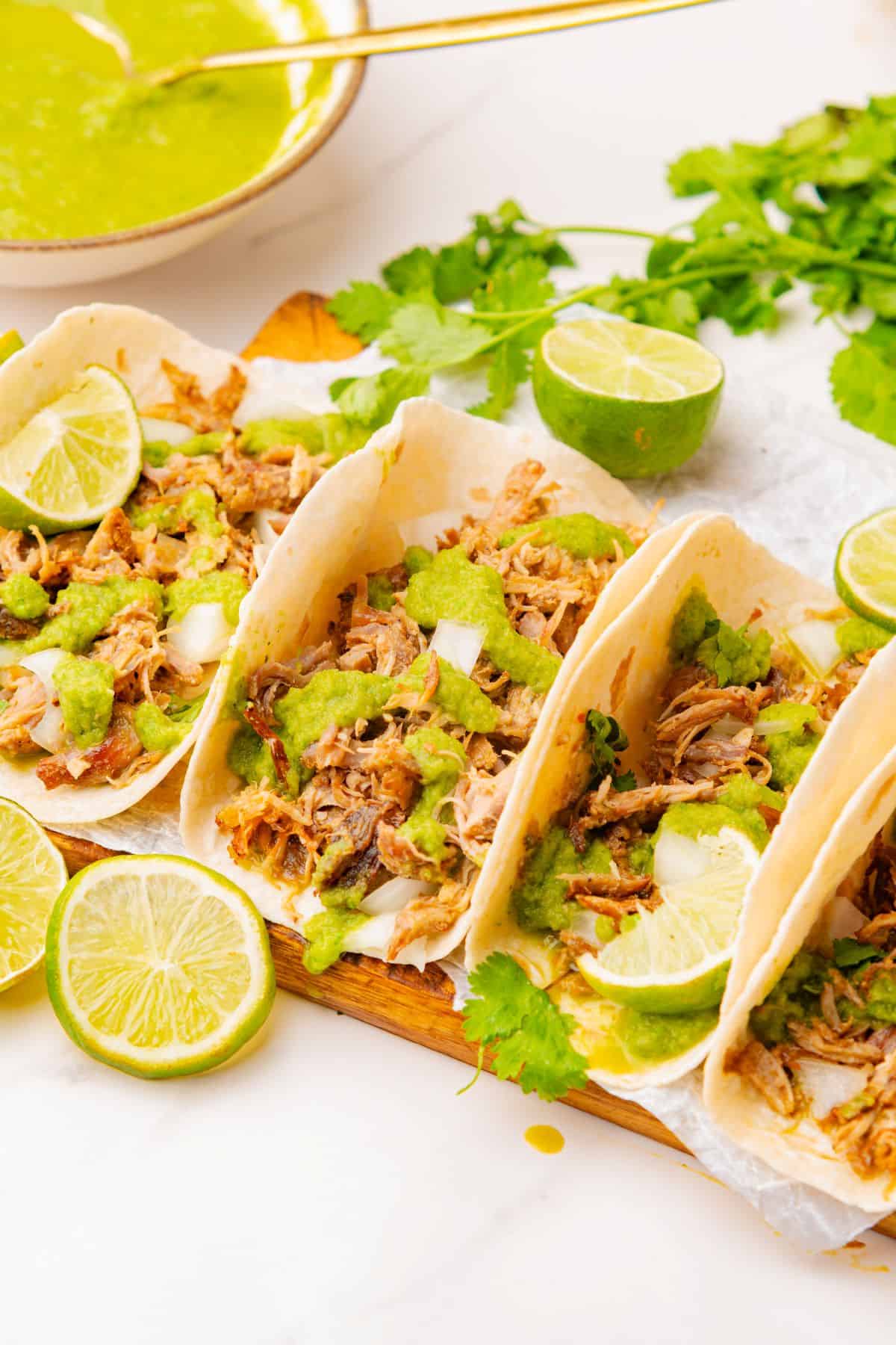 Three carnitas street tacos drizzled with salsa verde on a platter.