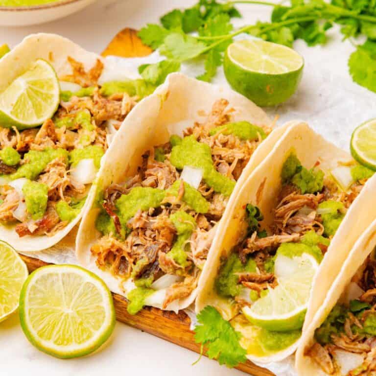 Three carnitas street tacos drizzled with salsa verde on a platter.