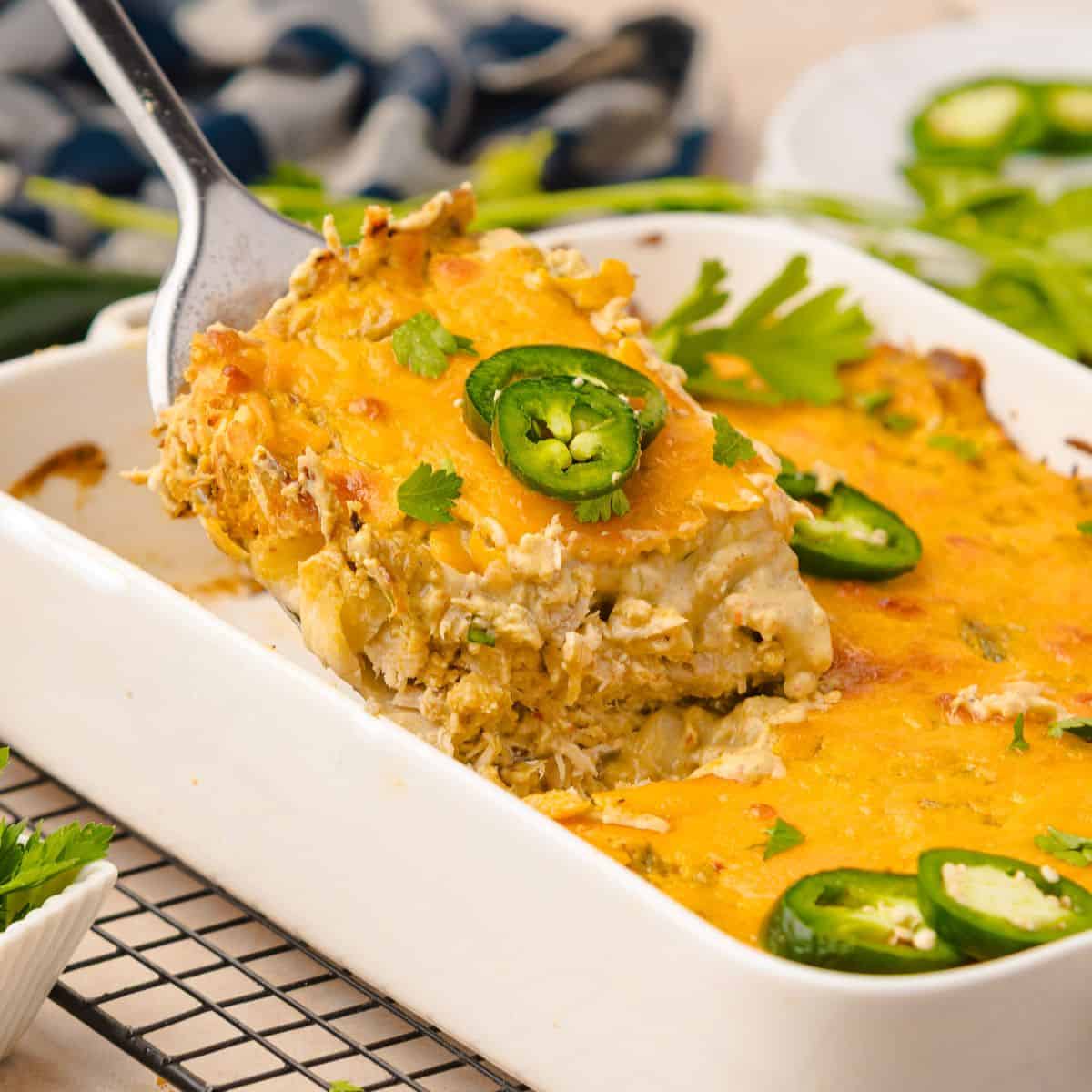 Chicken casserole in a white baking dish. A metal spatula is removing a slice from the dish.