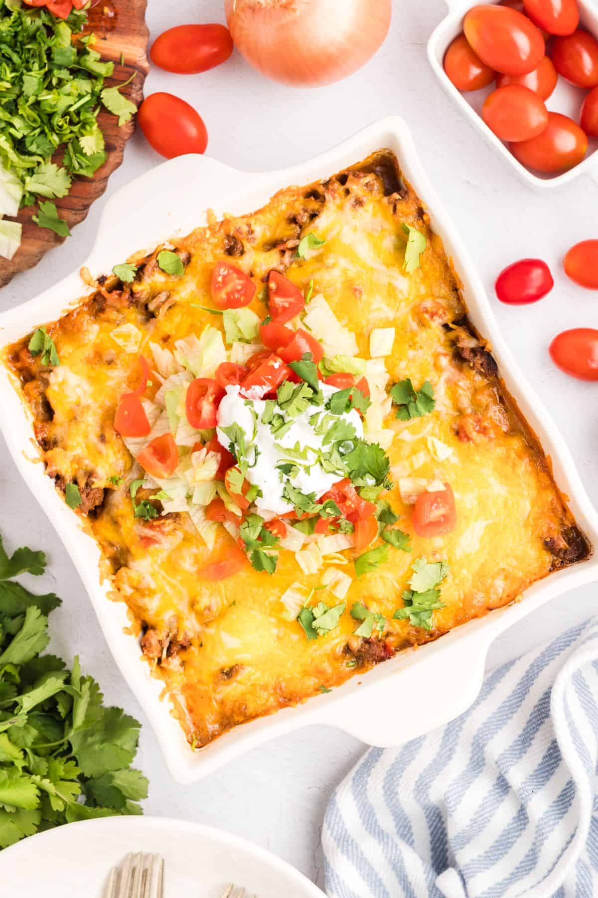 Taco lasagna in a baking dish topped with sour cream, tomatoes, and green onions.