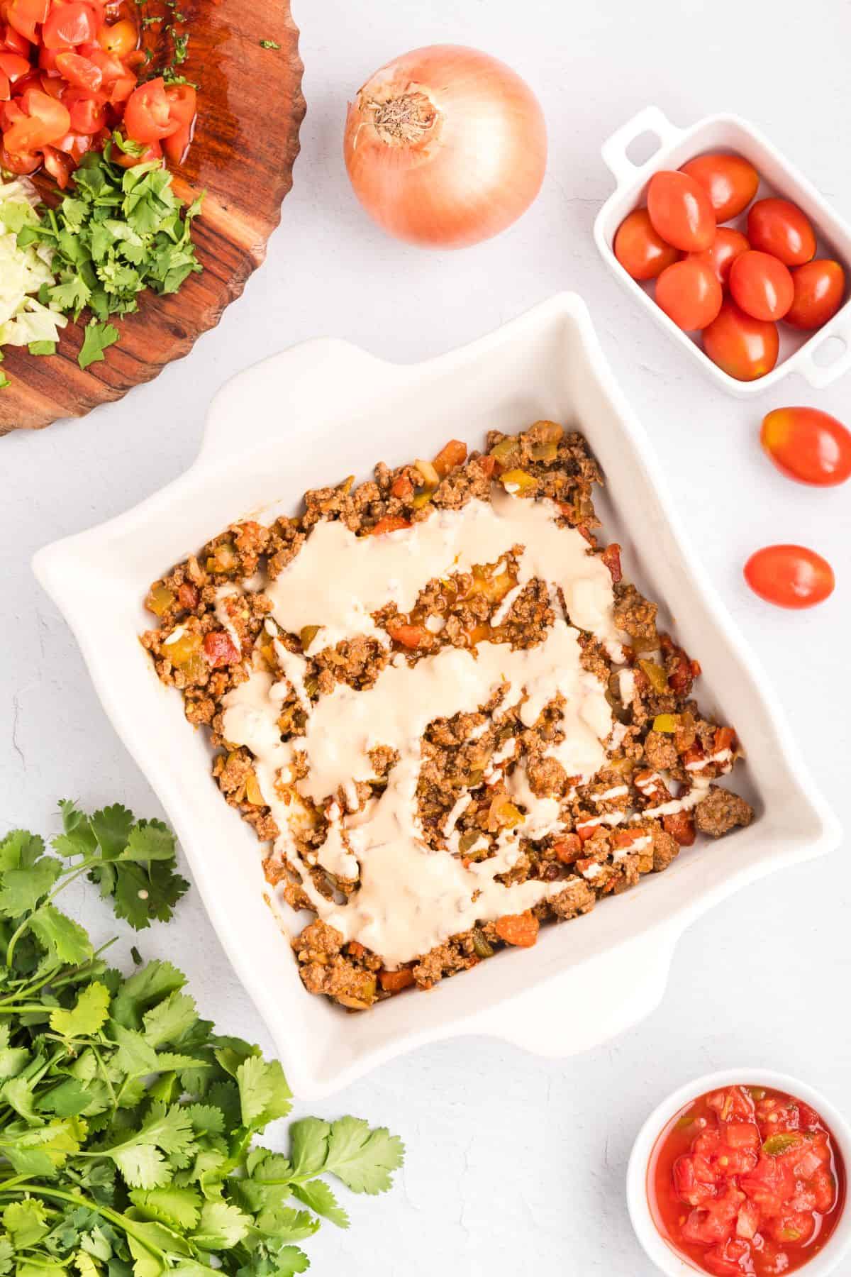 Baking dish with a layer of flour tortilla, ground beef, and queso.