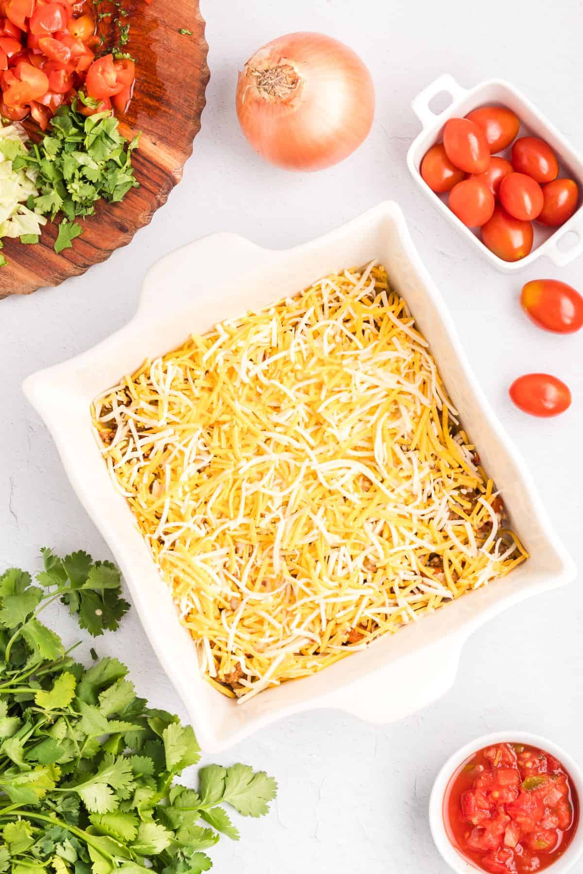 Baking dish with layers of flour tortillas, ground beef, queso, and shredded cheese.