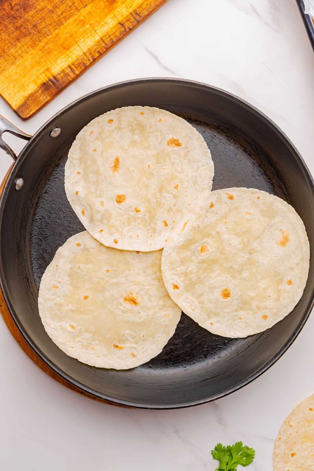 Three tortillas dry roasting in a skillet.