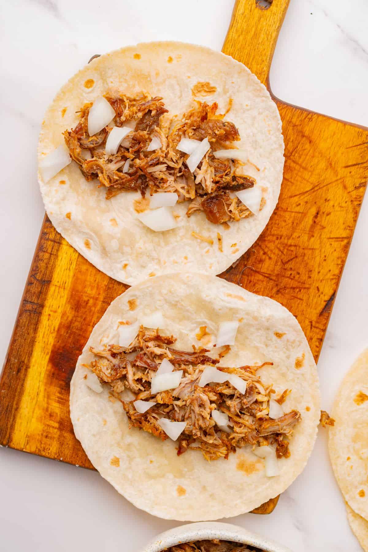 Tortillas filled with carnitas and diced white onions.