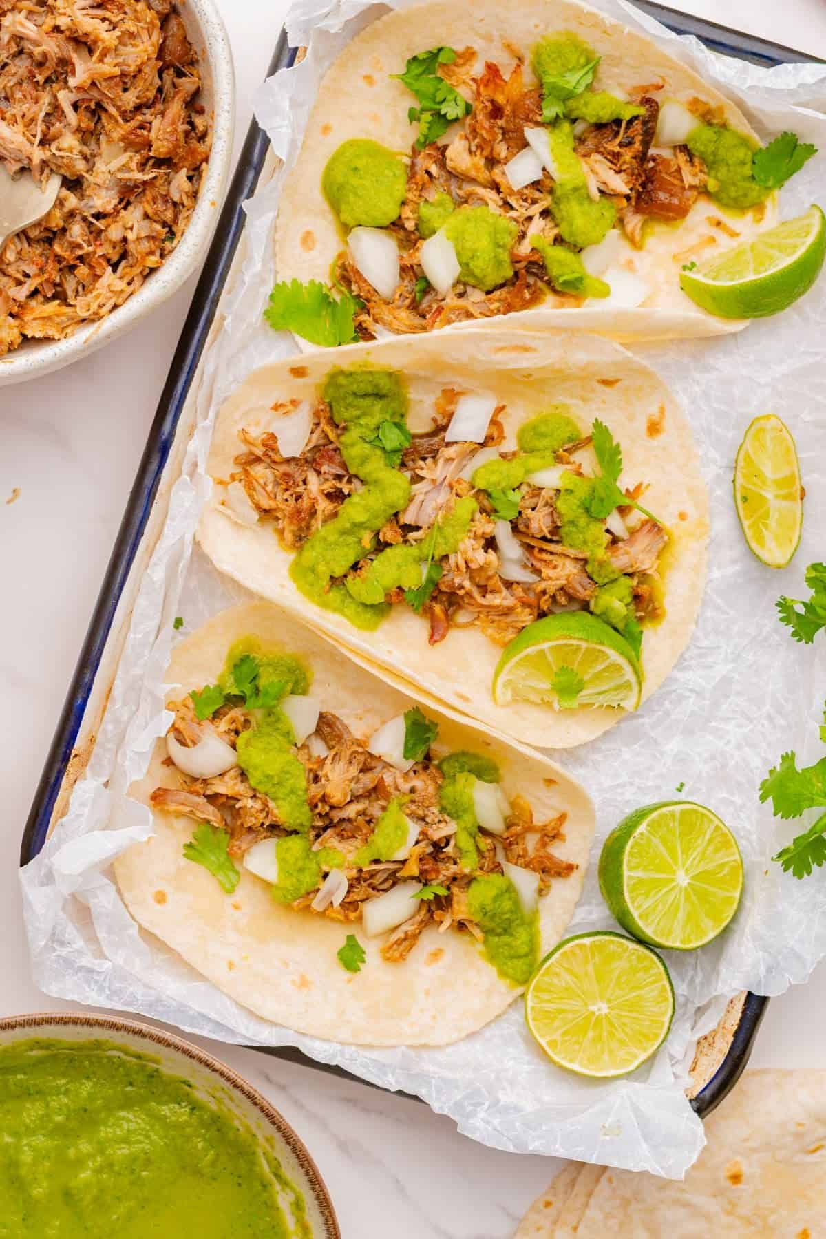Three carnitas with salsa verde and diced white onions.