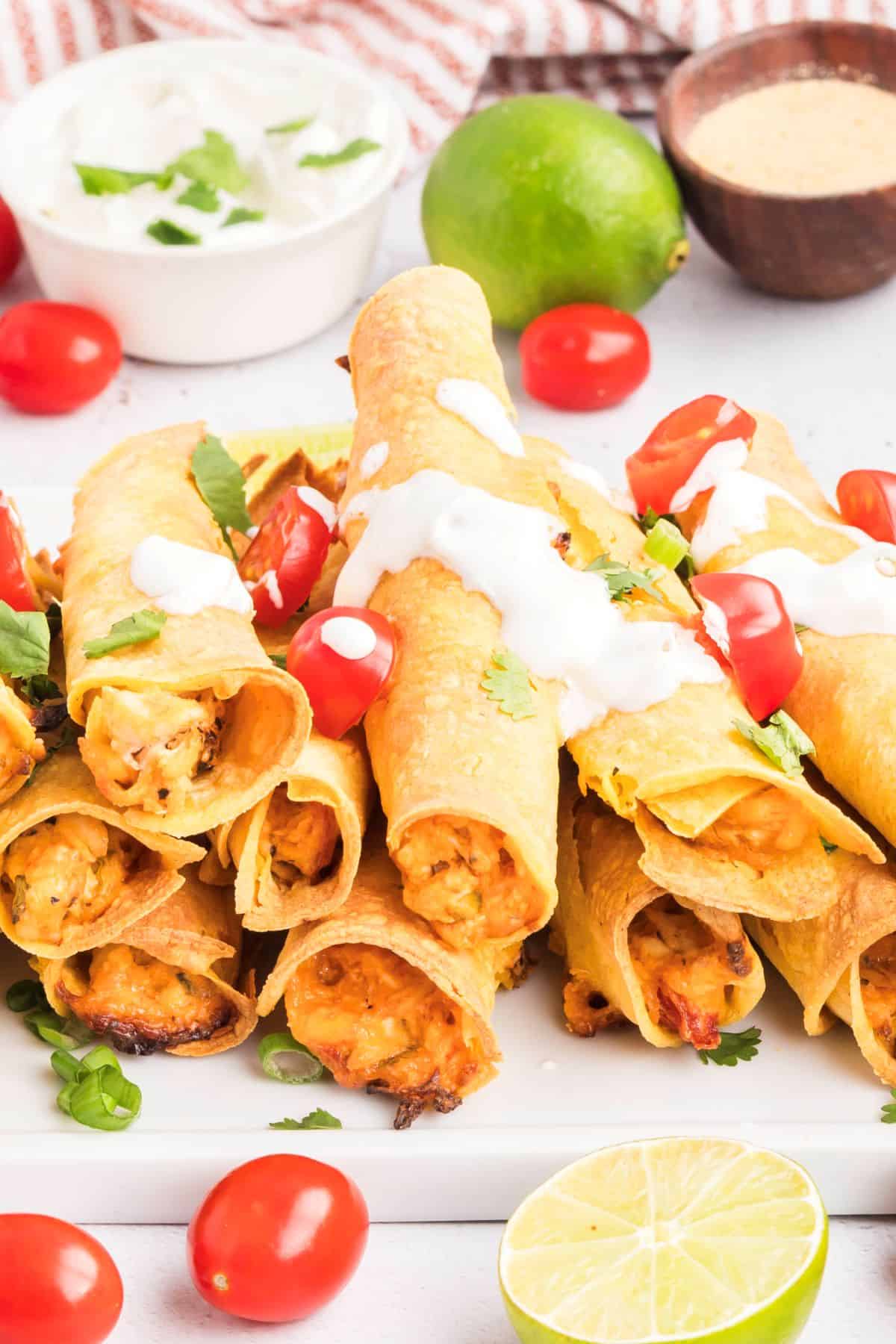 Baked chicken taquitos with cream cheese filling on a serving platter topped with sour cream and tomatoes.