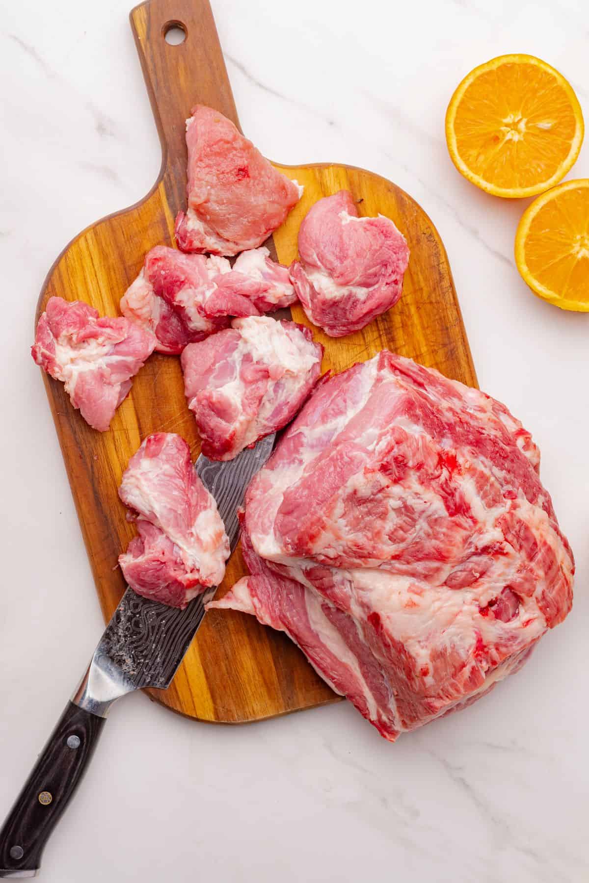Pork shoulder on a cutting board cut into 3 inch chunks.