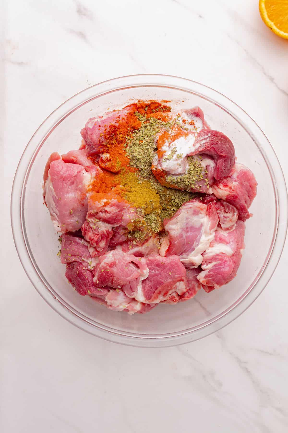 Chunks of pork shoulder and seasonings in a mixing bowl.