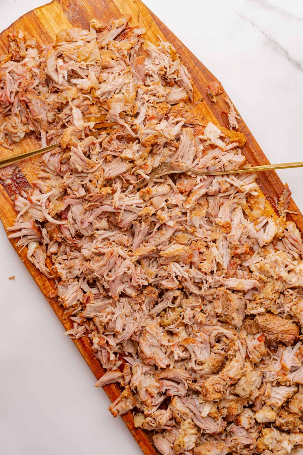 Two forks shredding pork carnitas on a cutting board.
