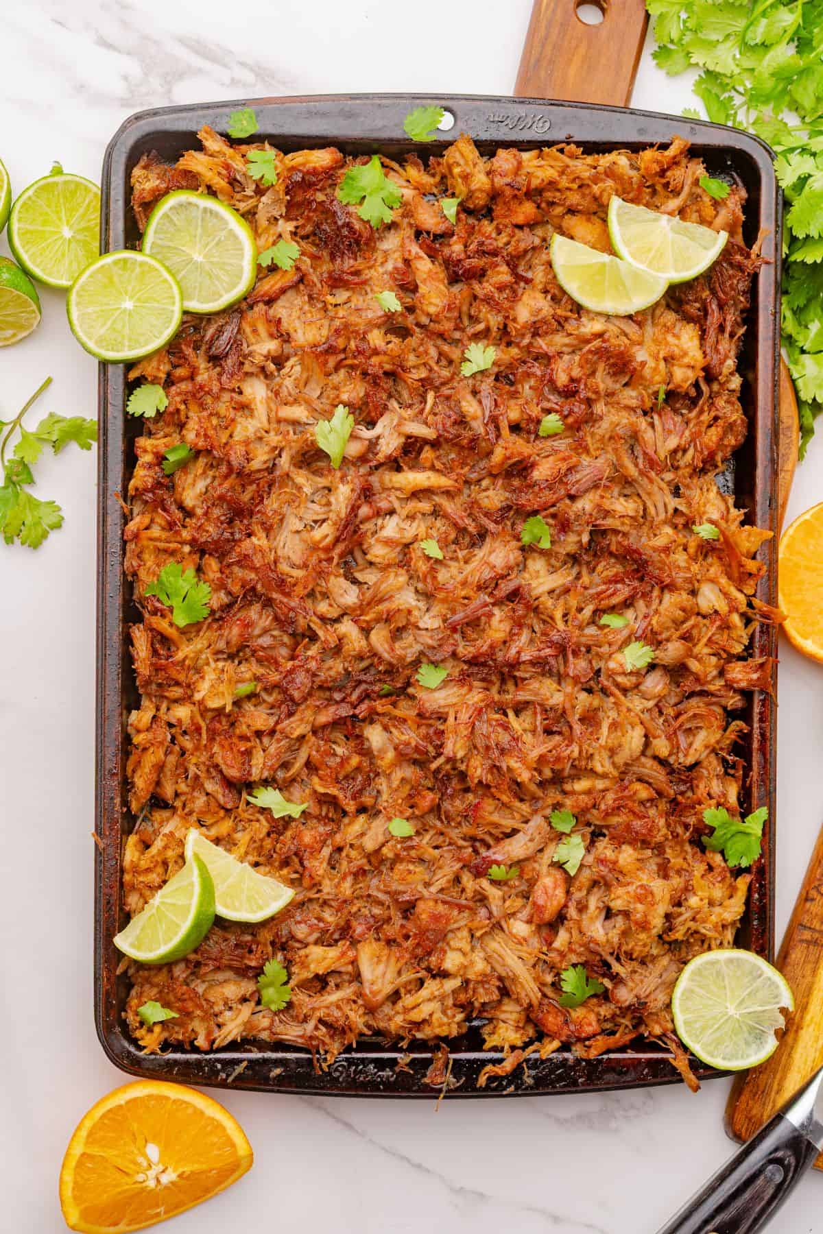 Shredded pork carnitas on a sheet pan with lime slices.