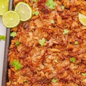 Shredded pork carnitas on a sheet pan with lime slices.