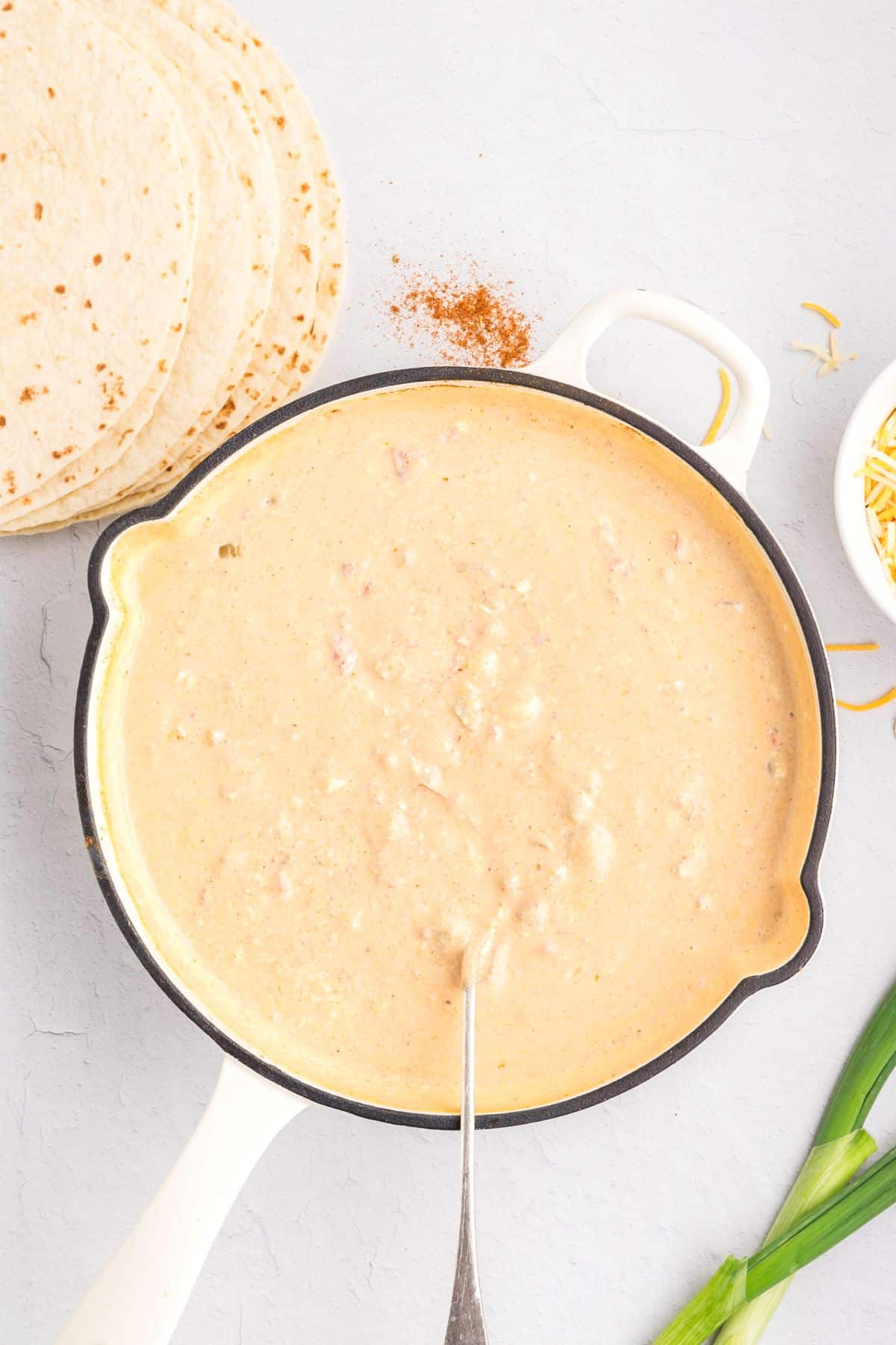 Cream cheese enchilada sauce in a skillet with a spoon.