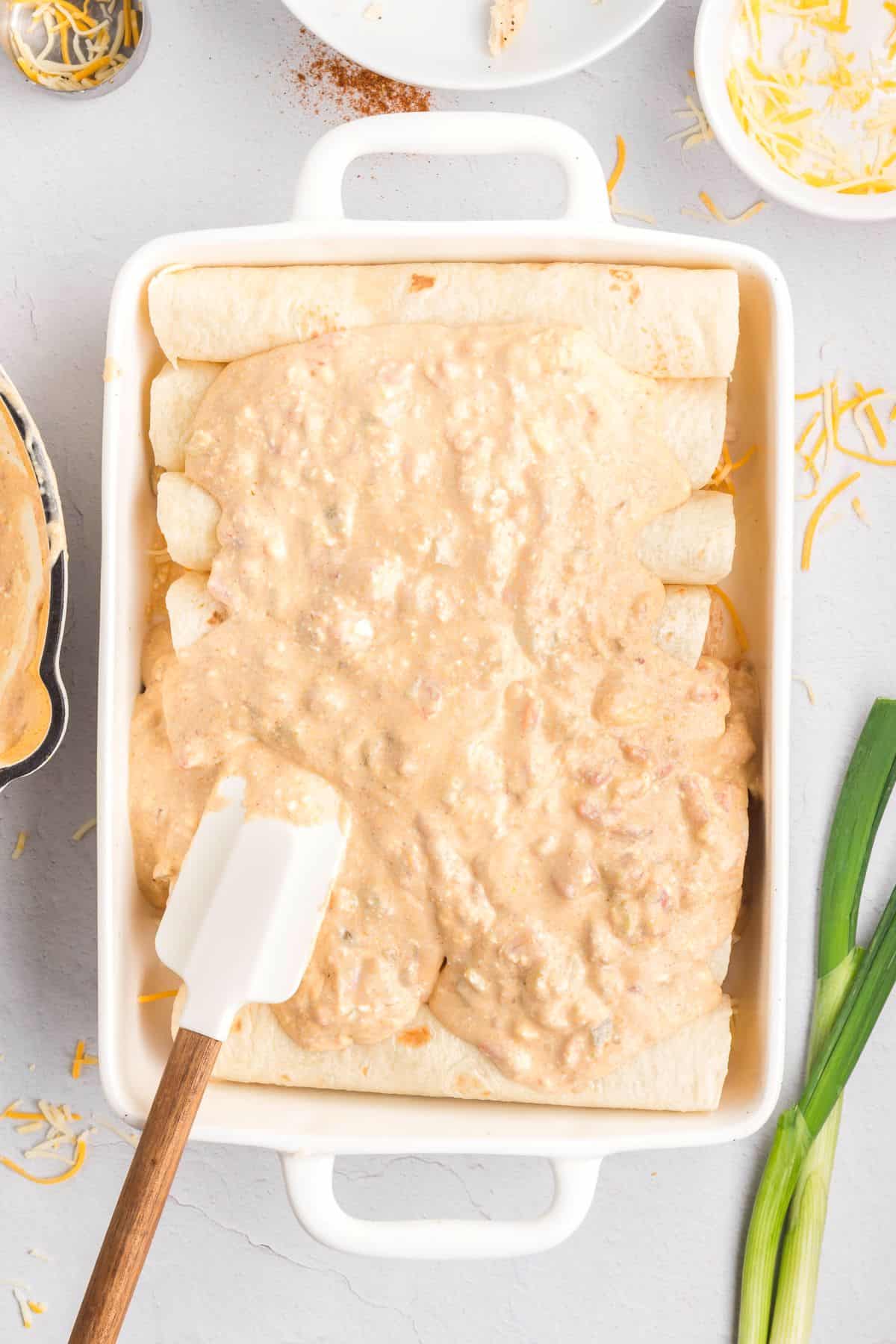 Chicken enchiladas with cream cheese sauce with a spatula in a baking dish.