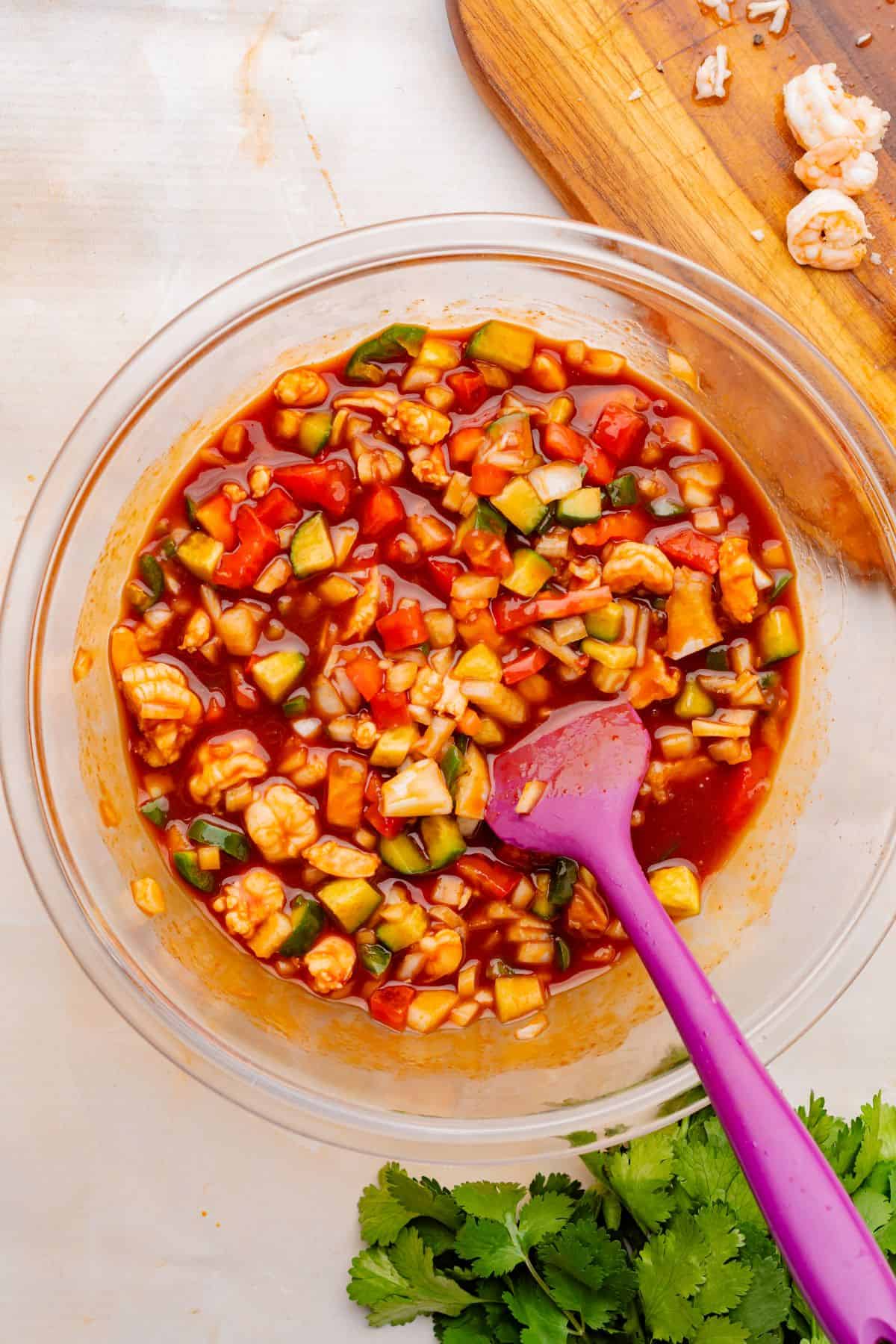 Mexican shrimp cocktail ingredients combined in a mixing bowl with a spatula.