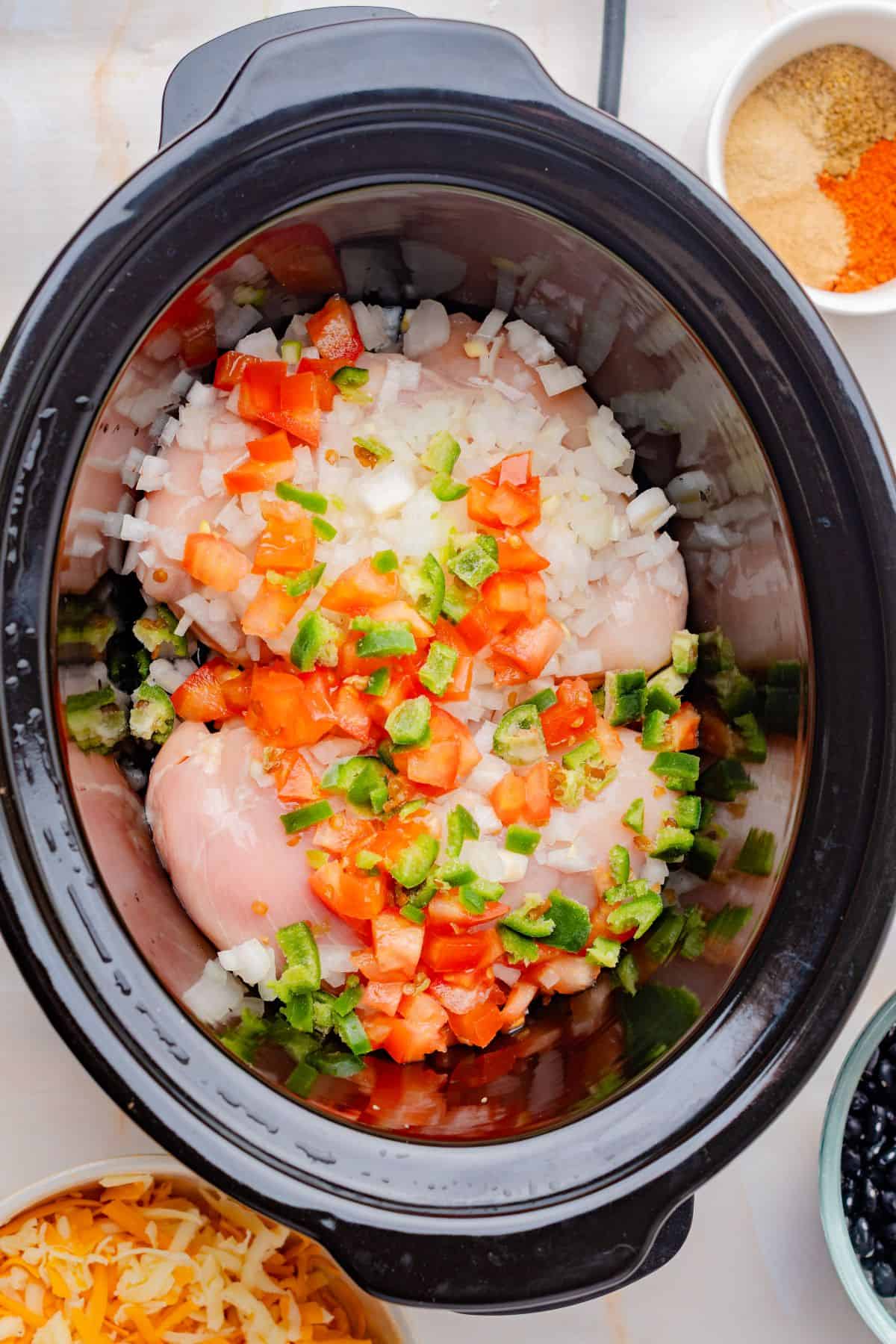 Chicken breasts, onions, and bell peppers in a slow cooker.