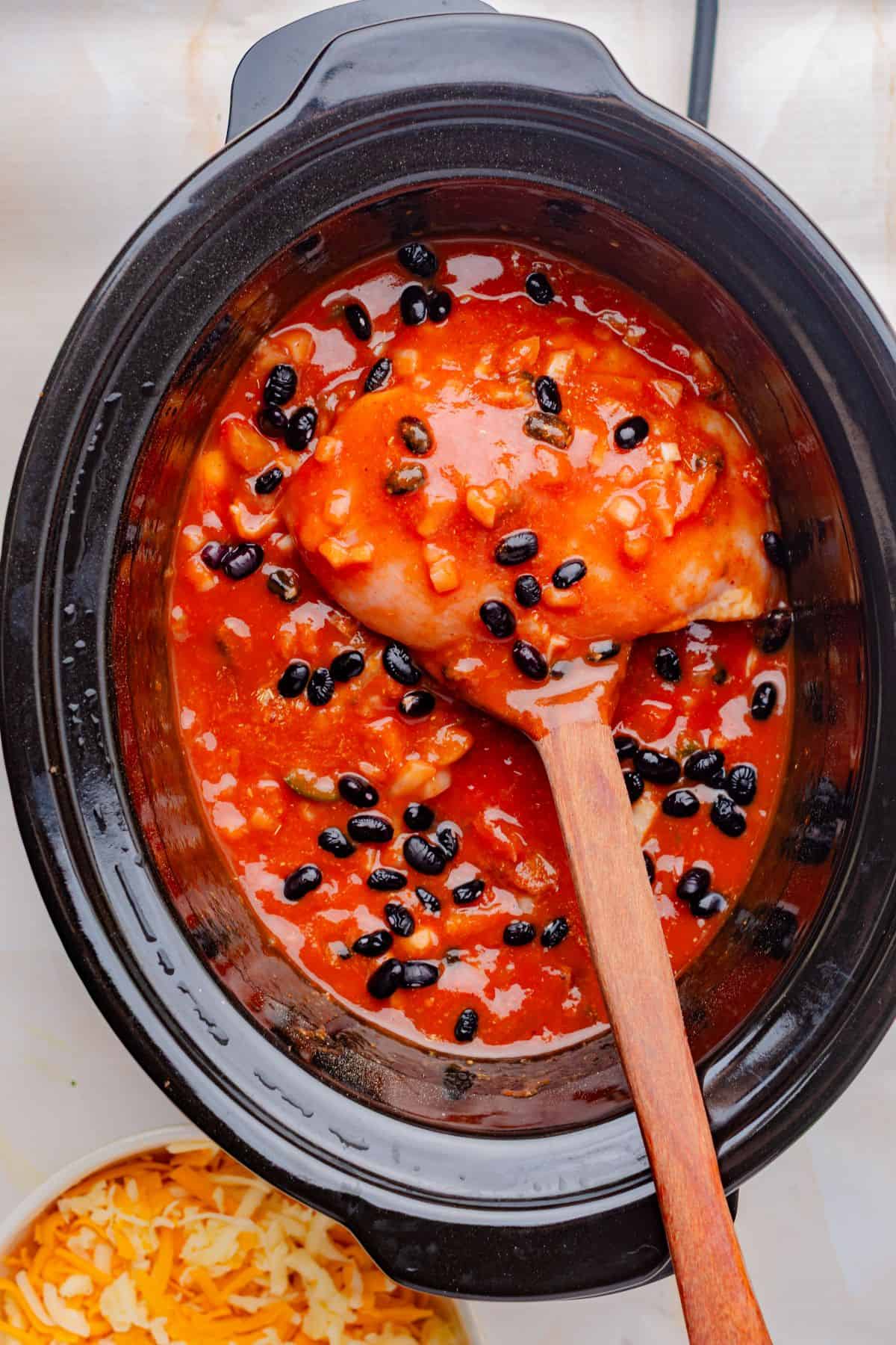 Chicken breasts in a slow cooker with red enchilada sauce and black beans.