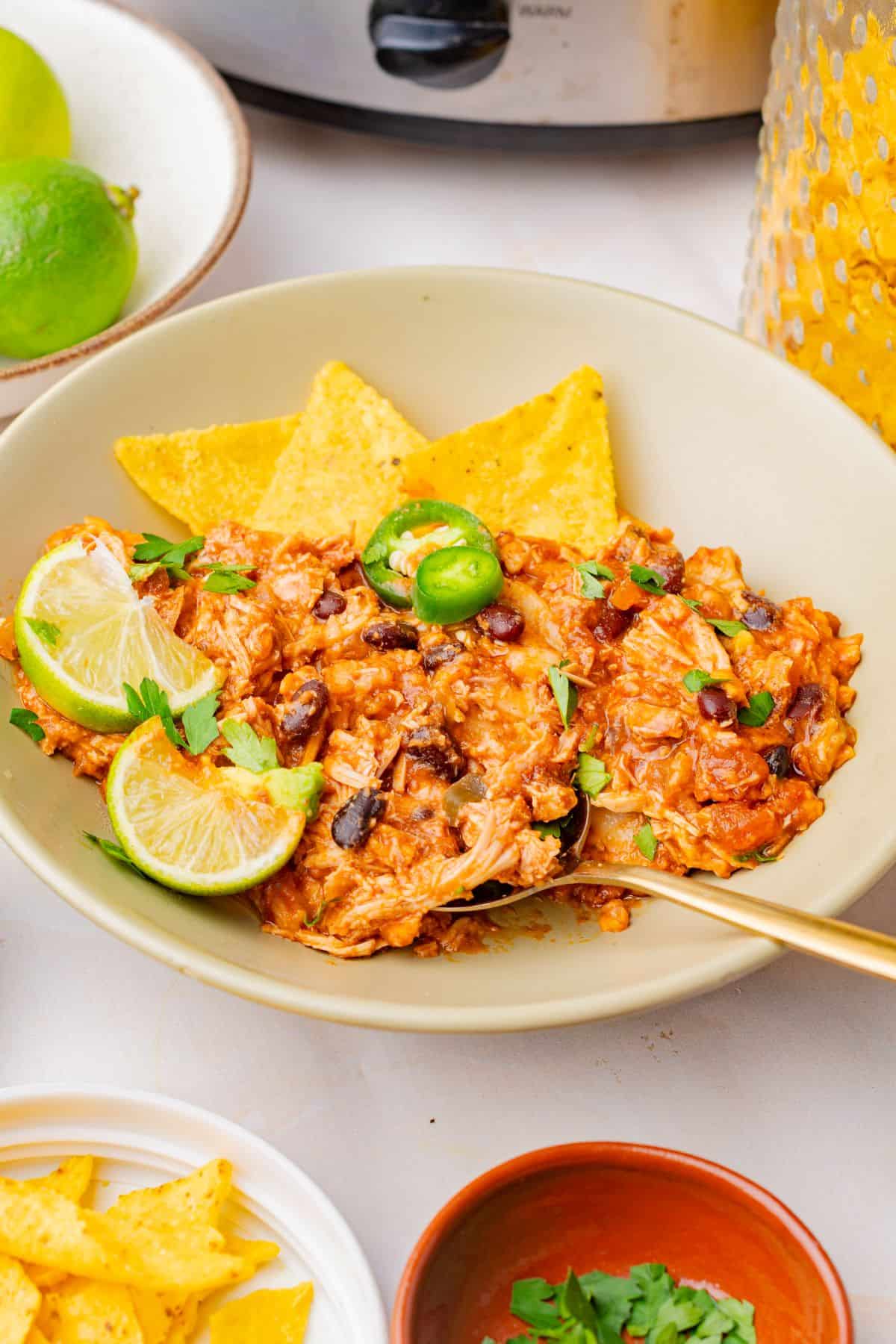 Slow cooker chicken enchiladas in a bowl with tortilla chips and a spoon.