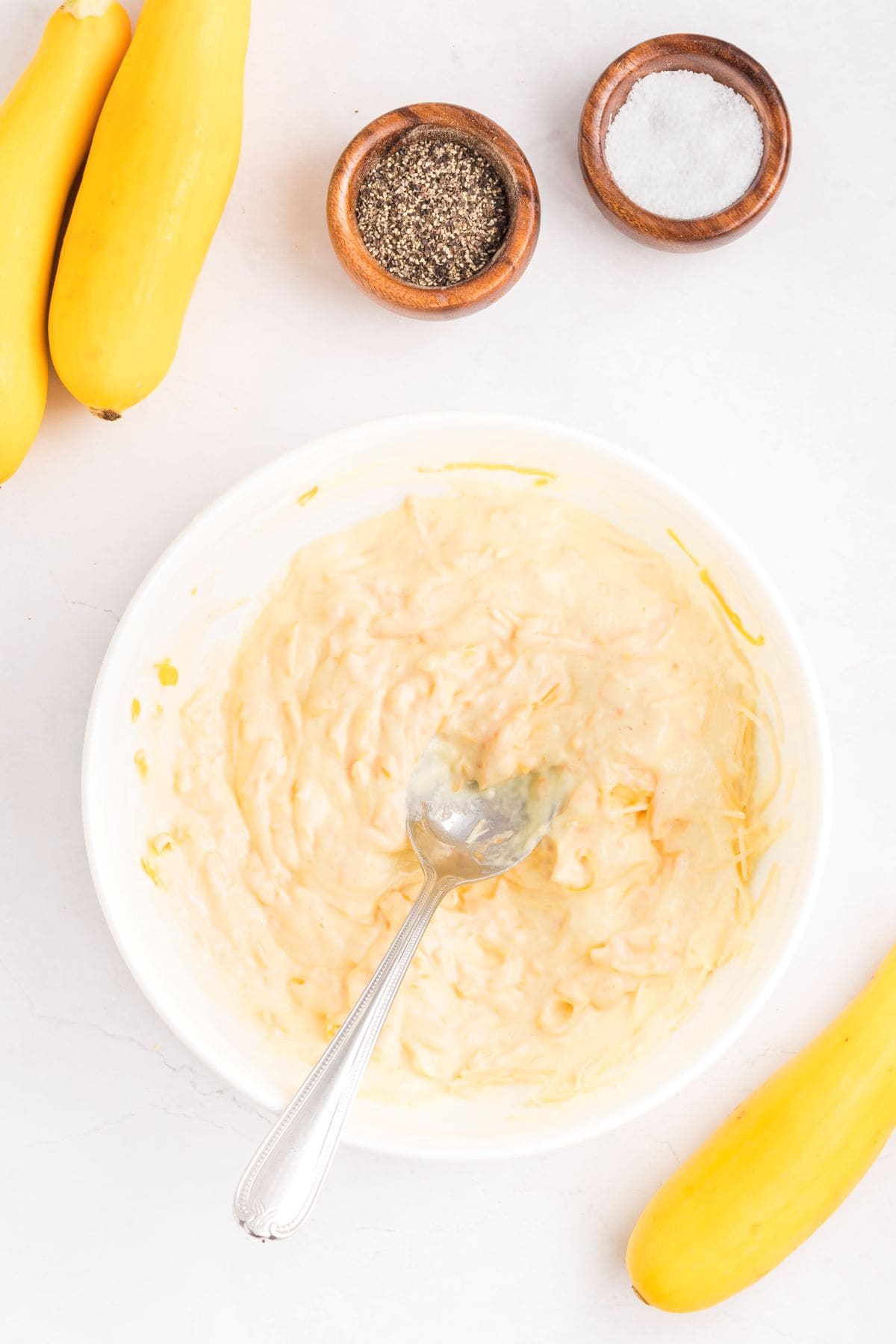 A mixing bowl with sour cream, mayo, eggs, and cheese mixed together with a spoon.